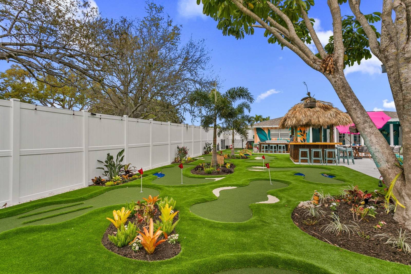 Backyard mini golf putting green with tropical plants and a tiki hut, installed by ProTurf Solutions